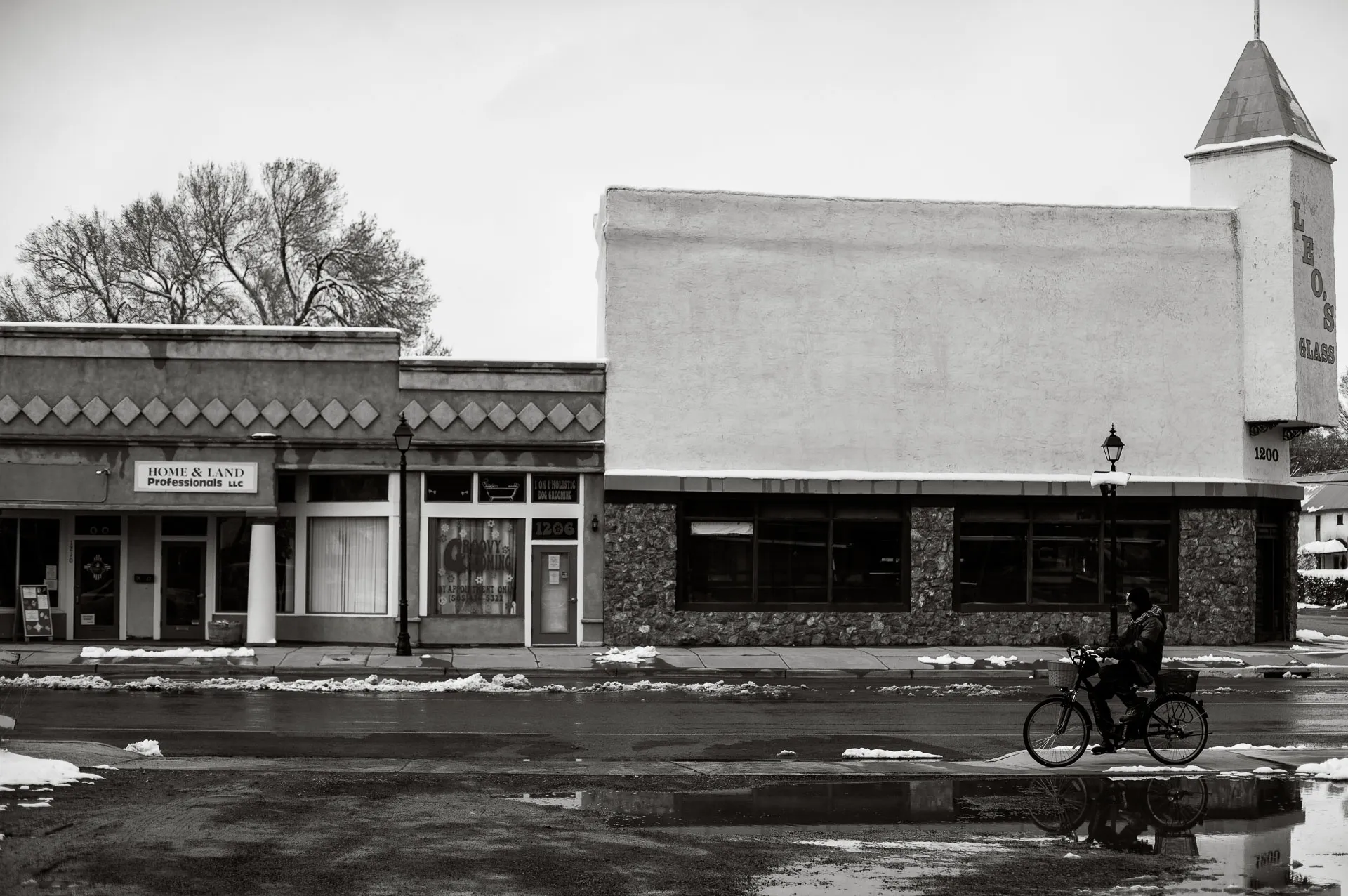 black and white photo of building on a main street with a man riding a bike in front.